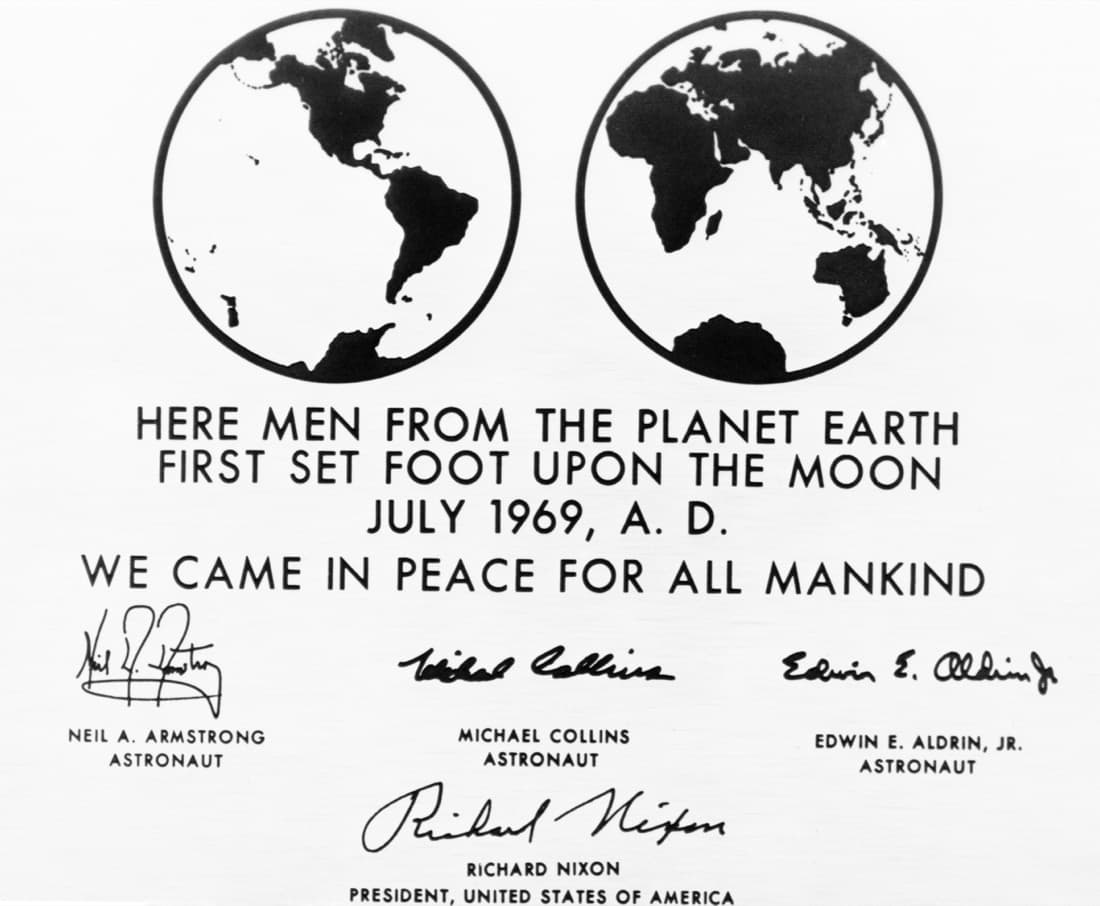 Black-and-white photograph of a plaque: two circles with the Earth's western and eastern hemispheres, then the words Here men from the planet Earth first set foot upon the Moon, July 1969, A. D. We came in peace for all mankind, and the signatures of Neil A. Armstrong, Michael Collins, Edwin E. Aldrin Jr. and Richard Nixon.